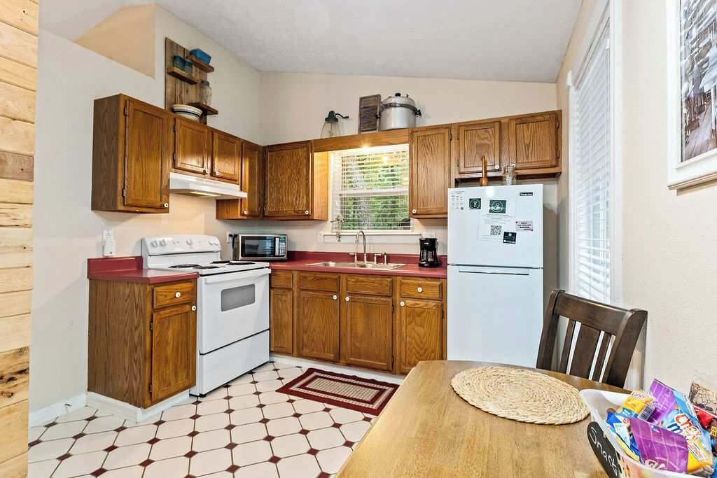 A compact kitchen with wooden cabinets, a microwave, a stove, a refrigerator, and a dining table with a placemat.