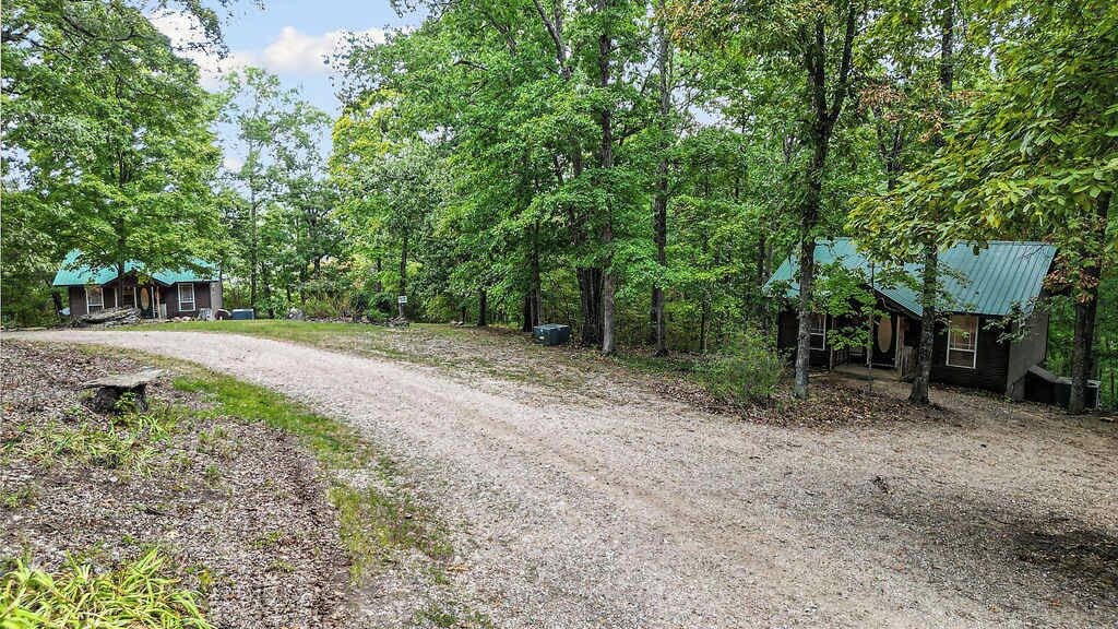 A gravel driveway leading to a cabin with a green roof, surrounded by dense trees.