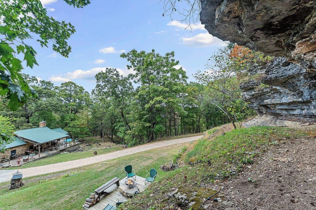 A rustic cabin with a green roof, surrounded by a forested area and a rocky cliff.
