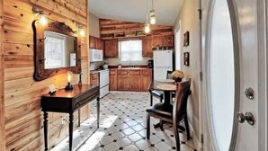 A compact kitchen with wooden walls, a tiled floor, and a dining area with a table and chairs. - Ozark Spring Cabin 04 Firefly Glow, King, Spa Tub (Eureka Springs)