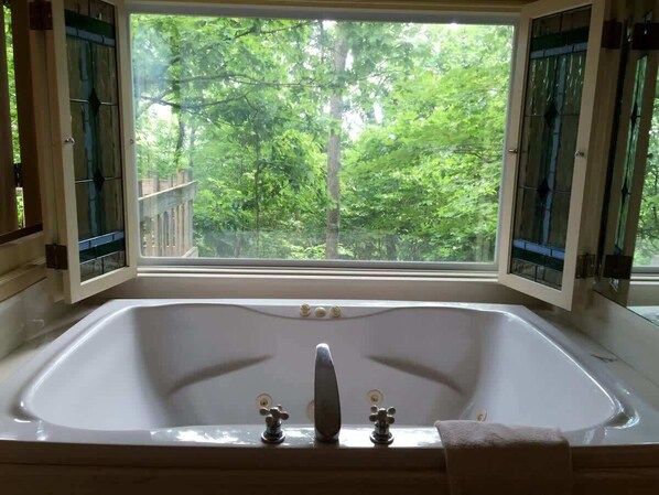 Eine große Badewanne mit Blick auf einen Wald durch ein Fenster.