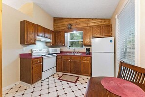 A compact kitchen with wooden cabinets, a microwave, a stove, and a refrigerator. - Romantic Ozark Cabin | Spa Tub • Trails • Cave (Eureka Springs)