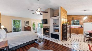 A bedroom with a bed, a ceiling fan, a fireplace, and a TV.