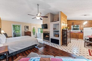 A bedroom with a bed, a ceiling fan, a fireplace, and a TV. - Romantic Ozark Cabin | Spa Tub • Trails • Cave (Eureka Springs)
