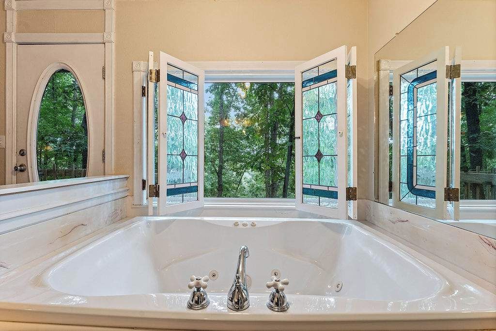 A large bathtub with a view of trees through open doors.