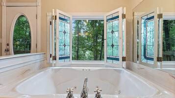 A large bathtub with a view of trees through open doors.