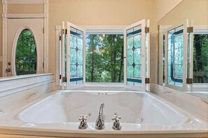 A large bathtub with a view of trees through open doors. - Romantic Ozark Cabin | Spa Tub • Trails • Cave (Eureka Springs)