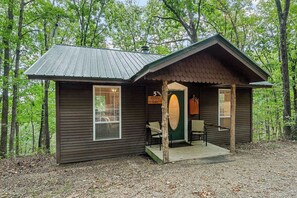 A cabin with a porch, a door, and a window. - Romantic Ozark Cabin | Spa Tub • Trails • Cave (Eureka Springs)