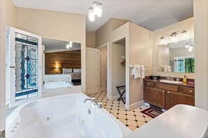 A bathroom with a large bathtub, wooden cabinets, a mirror, and a tiled floor. - Romantic Ozark Cabin | Spa Tub • Trails • Cave (Eureka Springs)