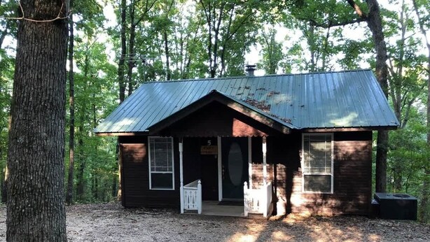 A rustic cabin with a metal roof, a porch, and a door leading to the interior.