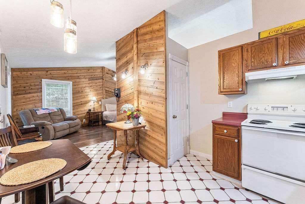 A compact living space with a dining area, a sofa, a kitchen with wooden cabinets, and a white stove.