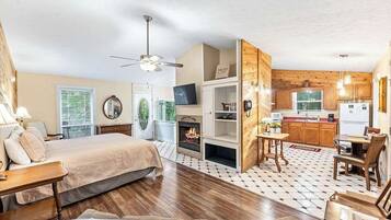 Quarto com cama, lareira, televisão e cozinha compacta.