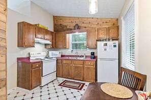 A compact kitchen with wooden cabinets, a microwave, a stove, and a refrigerator. - Romantic Cabin for Two | King Bed + Jetted Tub (Eureka Springs)