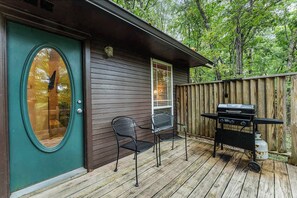 A wooden deck with a grill and chairs, a door with a window, and a wooden fence.