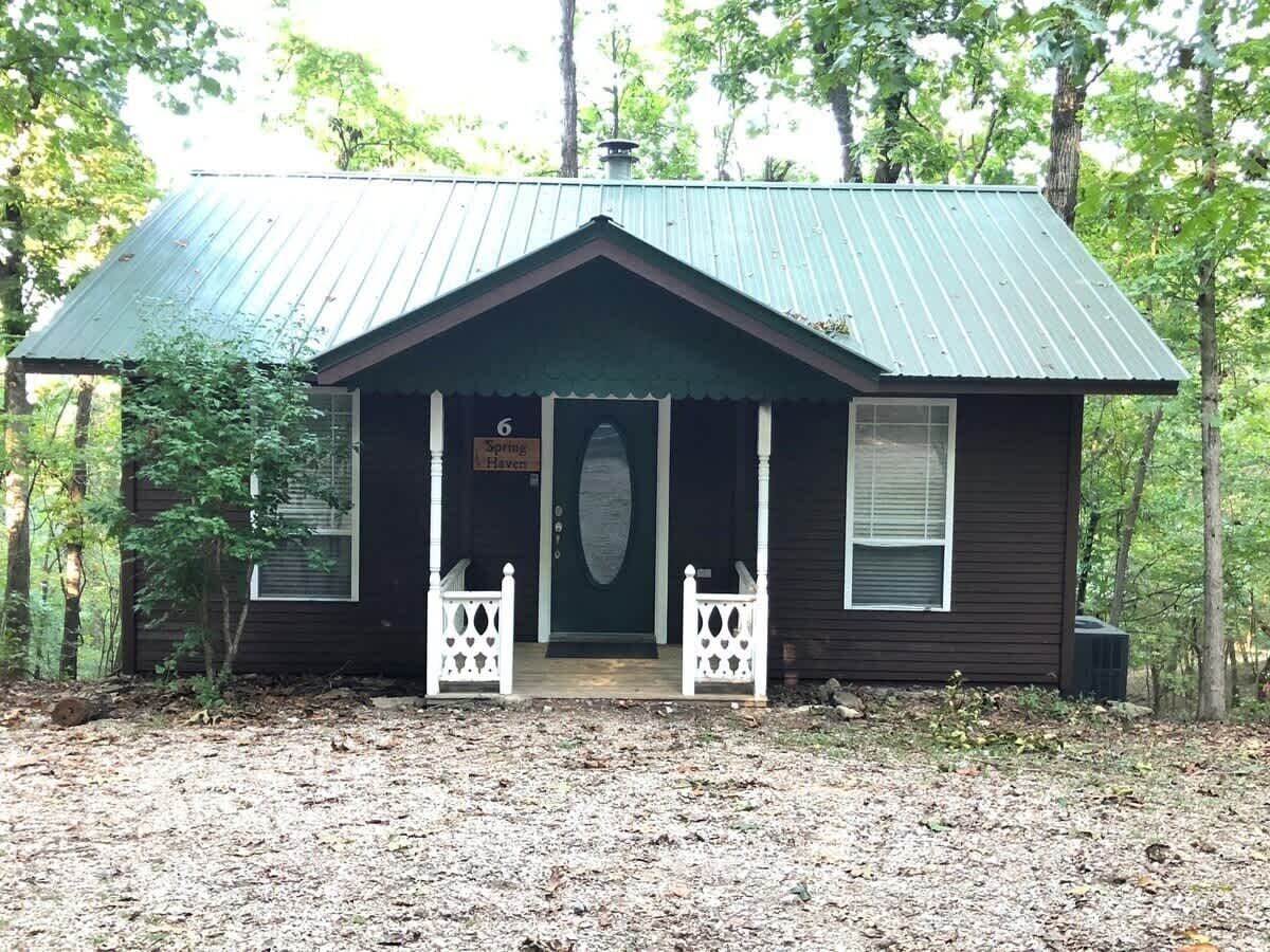 A small cabin with a green metal roof, a front porch with white railings, and a sign that reads 'Spring Haven.'