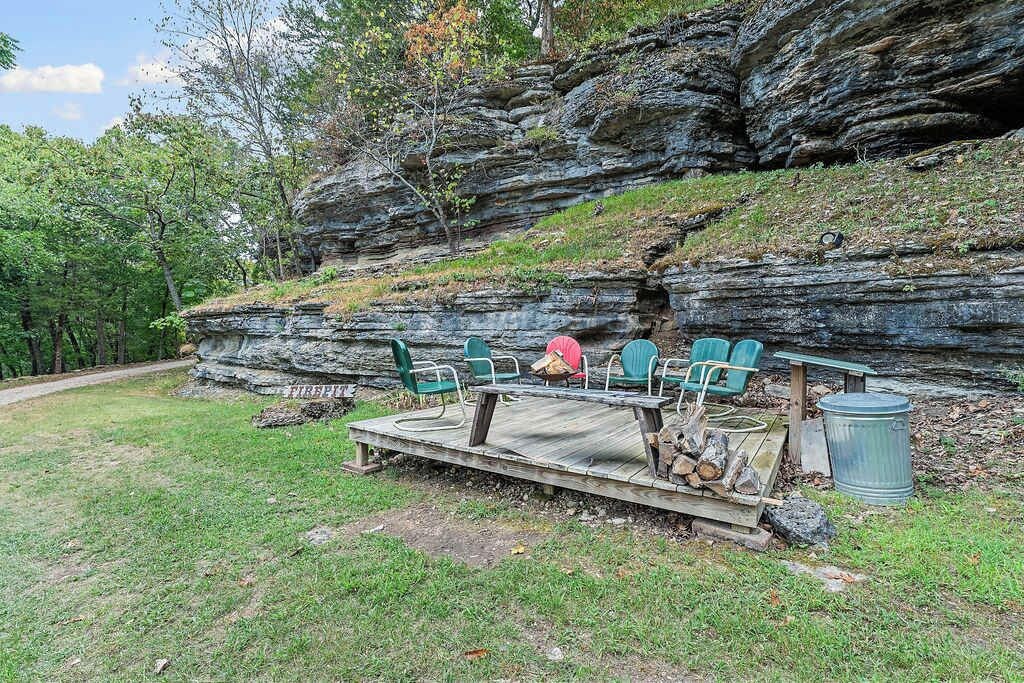 A rustic outdoor seating area with a wooden deck, green chairs, and a fire pit.