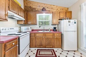 A compact kitchen with wooden cabinets, a white stove, a microwave, and a refrigerator.