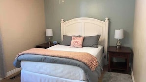 Een slaapkamer met een bed, twee nachtkastjes, een vloerkleed en een plafondventilator.