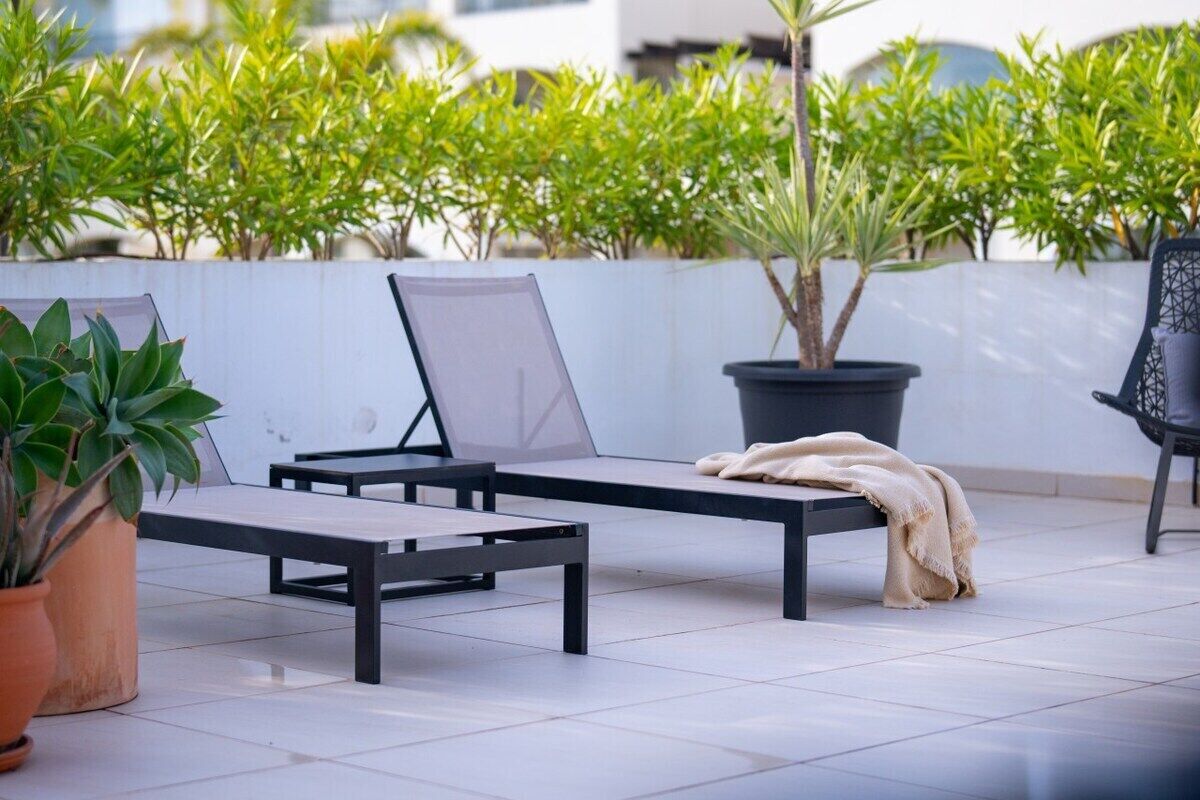 A patio area with two lounge chairs, a potted plant, and a bench.