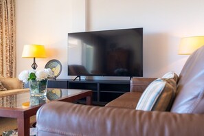 A living room with a leather sofa, a flat-screen TV, a coffee table, and two lamps.