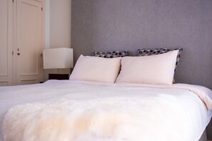 Een slaapkamer met een bed, kussens, een nachtkastje en een lamp.