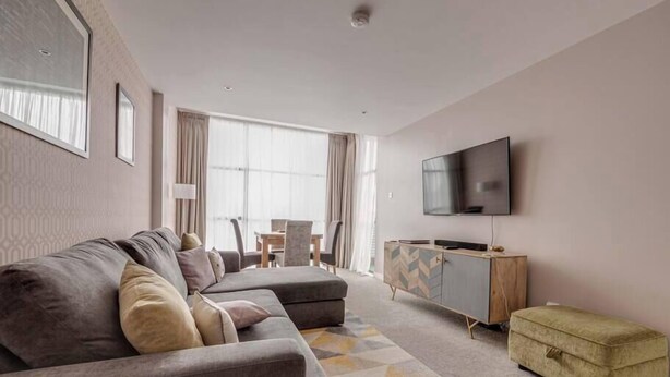 Una sala de estar moderna con un sofá gris, un televisor y un mueble con diseño de espiga.