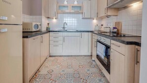 Una cocina moderna con armarios de madera clara, microondas, fregadero y baldosas de suelo estampadas.