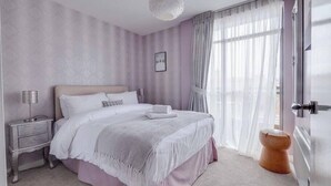 Un dormitorio con cama, mesitas de noche, lámpara, ventana con cortinas y puerta.