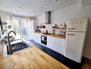 Eine moderne Küche mit weißen Schränken, einer Holz Arbeitsplatte, einem eingebauten Backofen, einer Edelstahl-Dunstabzugshaube und einem weißen Kühlschrank.