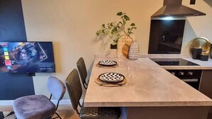 Een moderne keuken met een eettafel gedekt voor twee personen, een televisie aan de muur en een plant op de tafel.