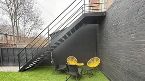 Een klein buitenruimte met kunstgras, een zwarte muur en een trap.
