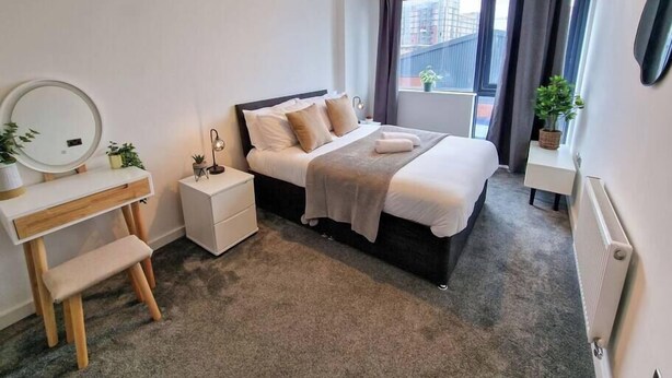 Een slaapkamer met een bed, nachtkastje, lamp, spiegel en uitzicht.
