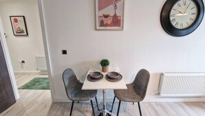 Een eetgedeelte met een tafel, twee stoelen, een klok en een ingelijste foto aan de muur.