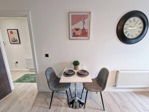 A dining area with a table, two chairs, a clock, and a framed picture on the wall. - 1 Bed Baltic Triangle Flat | Liverpool (Merseyside)