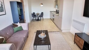 A modern living room with a sofa, coffee table, and a dining area with chairs and a table. - Media City Apartment (Greater Manchester)