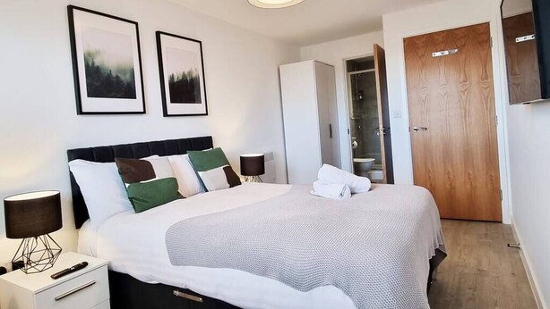 A neatly arranged bedroom with a bed, bedside tables, a wardrobe, and framed pictures on the wall. - Media City Apartment (Greater Manchester)