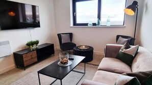 A modern living room with a flat-screen TV, a sofa, a coffee table, a side table, and a window with a view. - Media City Apartment (Greater Manchester)