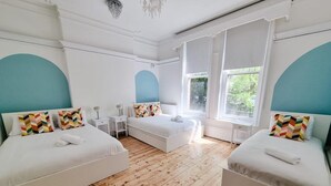 A room with two beds, a wooden floor, and large windows. - 6 Bed Mansion | Sleeps 20 | Free Parking (Ashton-under-Lyne)