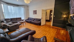 A spacious living room with a large sectional sofa, a smaller sofa, and a coffee table. There is a fireplace with a modern lamp, and a door leading to another room. - 6 Bed Mansion | Sleeps 20 | Free Parking (Ashton-under-Lyne)