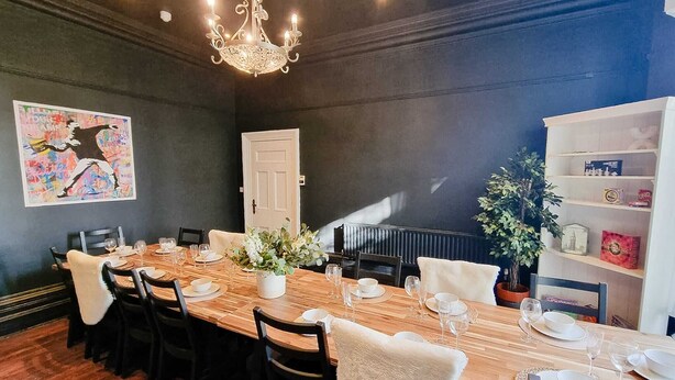 A dining area with a long wooden table, black chairs, a chandelier, a door, a plant, and a bookshelf. - 6 Bed Mansion | Sleeps 20 | Free Parking (Ashton-under-Lyne)