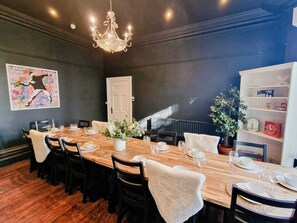 A dining area with a long wooden table, black chairs, a chandelier, a door, a plant, and a bookshelf. - 6 Bed Mansion | Sleeps 20 | Free Parking (Ashton-under-Lyne)