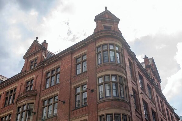 A corner of a red brick building with multiple windows and a triangular roof structure.