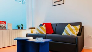 A modern living room with a dark sofa, two side tables, a bowl on one table, and a framed picture on the wall. - Paillette (Centre-Ville) (Le Havre)