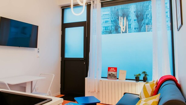A modern room with a bed, a TV, a table, and a window with curtains. - Paillette (Centre-Ville) (Le Havre)