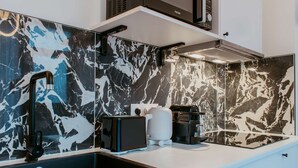 A modern kitchen with a black and white marble backsplash, a black faucet, a white kettle, and a coffee machine. - Paillette (Centre-Ville) (Le Havre)
