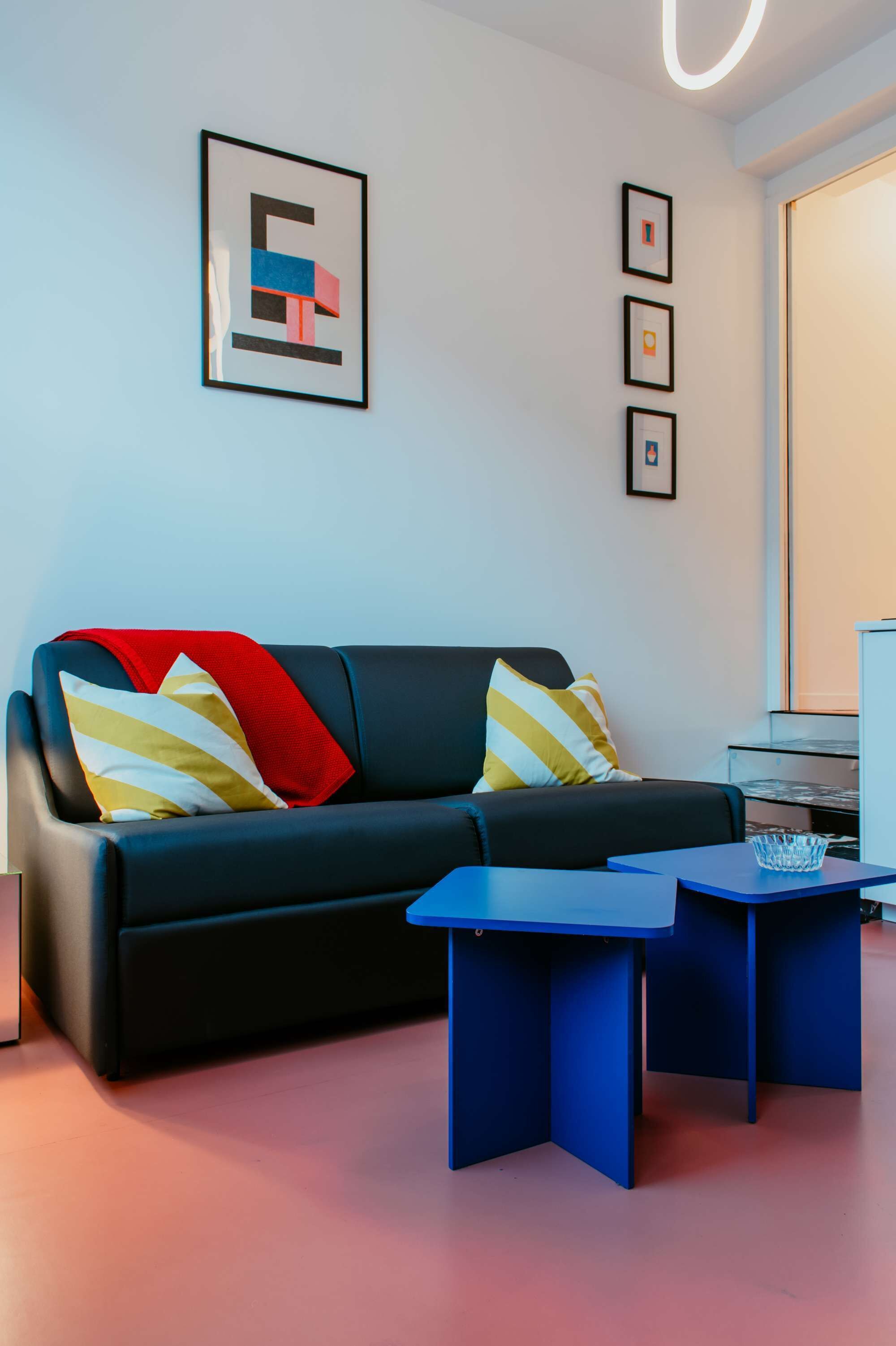 A modern living room with a dark sofa, two blue side tables, and a red and yellow striped throw blanket.