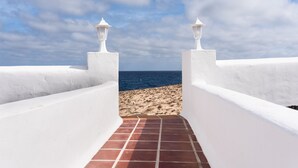Un camino que lleva a una playa con paredes blancas y tejas rojas, bajo un cielo parcialmente nublado.