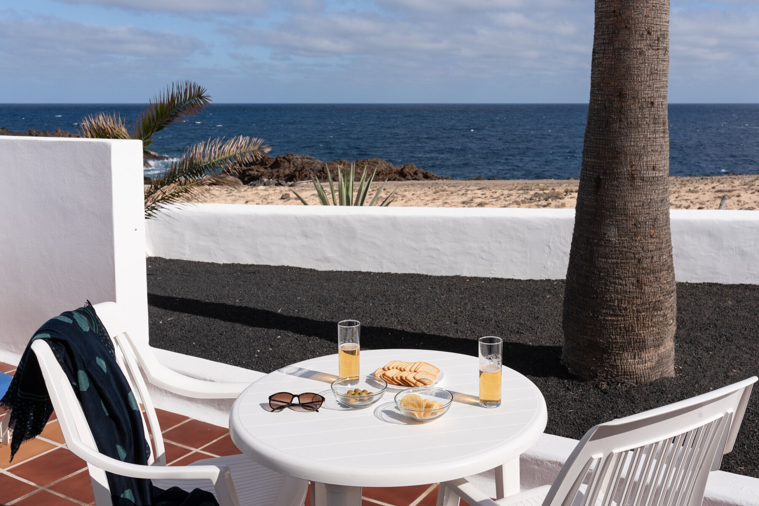 Een tafel met drankjes, snacks en zonnebrillen op een terras met uitzicht op de oceaan.