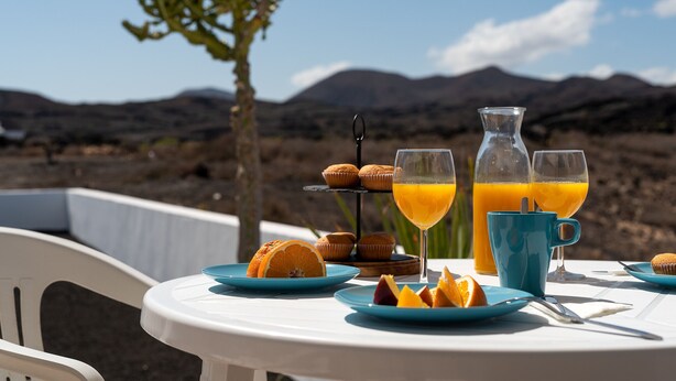 Ein Tisch ist reichhaltig mit Frühstück zubereitet, darunter Muffins, Orangenscheiben und Gläser Orangensaft, mit einer Berglandschaft im Hintergrund.