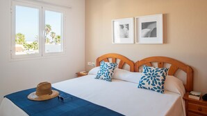 Una habitación de hotel con una cama, dos almohadas, un sombrero y gafas de sol sobre la cama. Hay dos cuadros en la pared.
